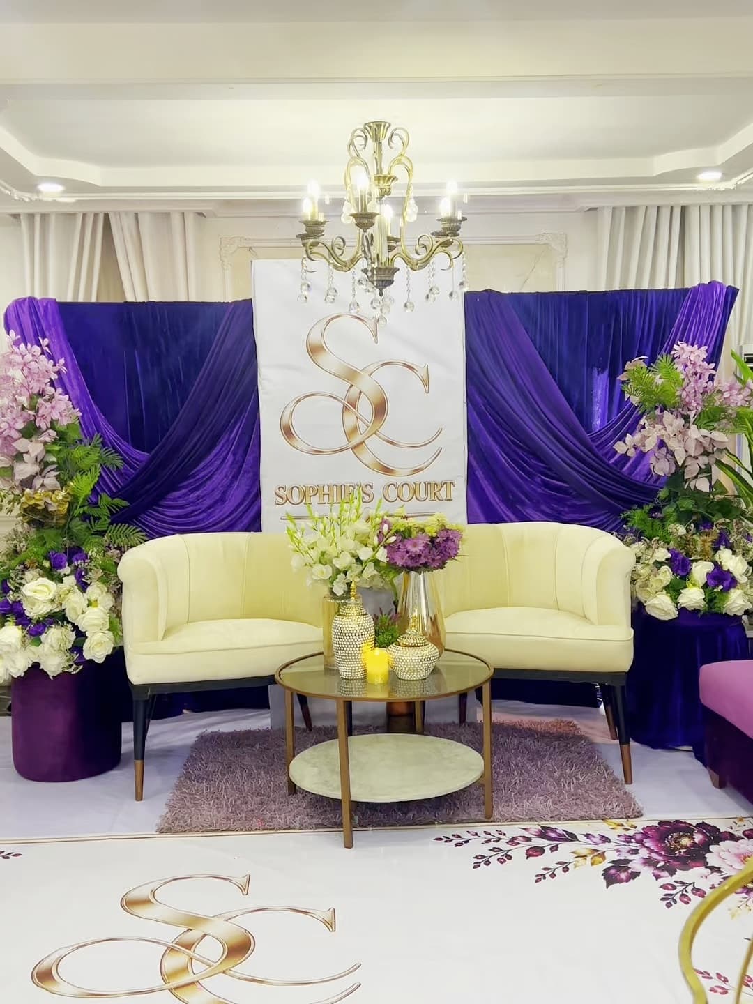 Cream armchairs before purple drapes and a Sophie's Court backdrop, set for a celebration